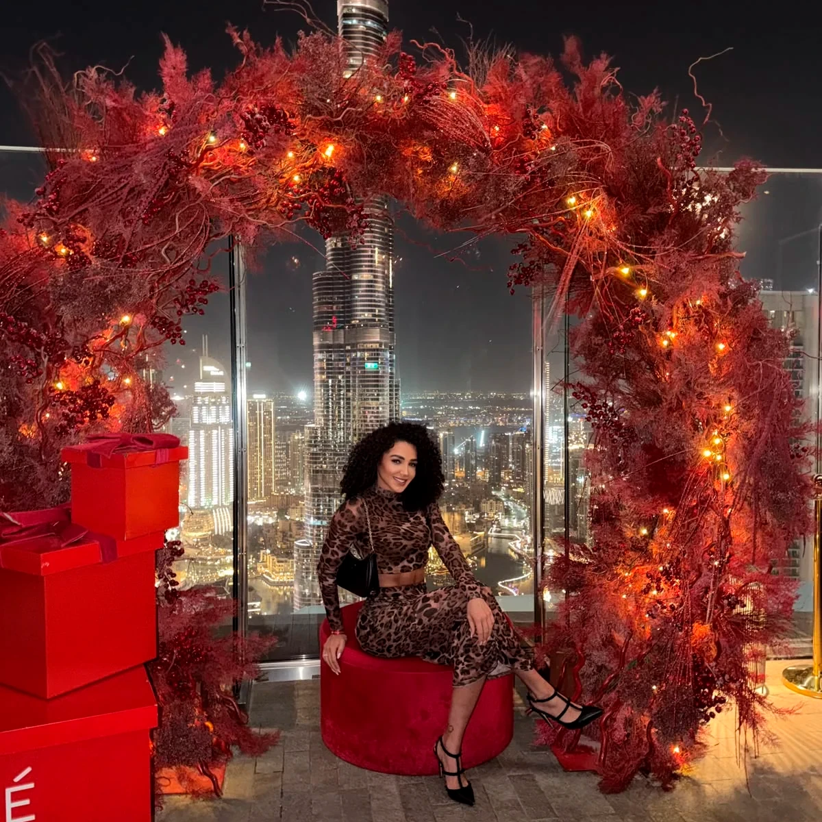 Larissa framed by a red floral installation above Downtown Dubai at night